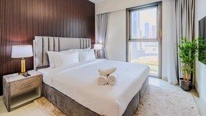 Ein modernes Hotelzimmer mit einem großen Bett, einem Nachttisch mit Lampe, Blick auf die Stadt durch das Fenster und einer Zimmerpflanze.