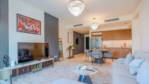 Ein modernes Wohnzimmer mit Fernseher, Sofa und Couchtisch. Ein Essbereich mit Stühlen und Tisch ist ebenfalls vorhanden. Im Hintergrund ist die Küche zu sehen.