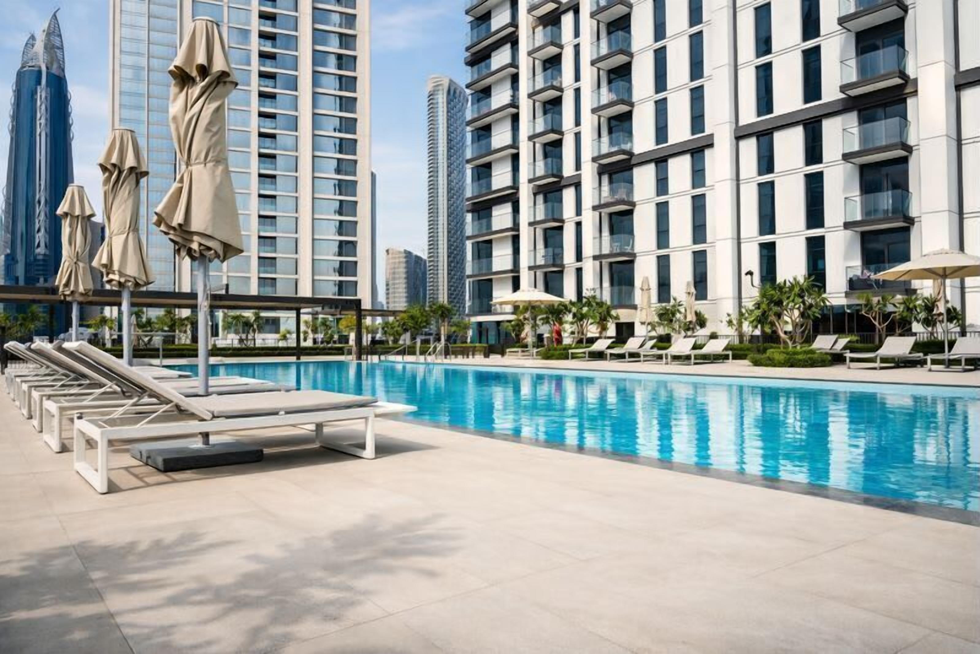 Un espace piscine avec des chaises longues et des parasols, entouré d’immeubles de grande hauteur.