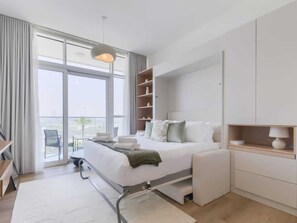 Ein modernes Hotelzimmer mit einem großen Bett, einem Nachttisch, einem Sessel, einem Schreibtisch und Blick ins Freie.