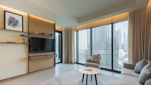 A modern living room with a flat-screen TV, a sofa, a coffee table, and large windows offering a city view. - Full Burj Khalifa View, Premium 3BR Furnished Unit (Dubai)