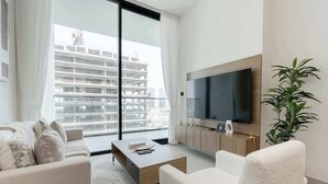 Ein modernes Wohnzimmer mit großem Fernseher, bequemen Sitzmöglichkeiten, einem Couchtisch und Blick auf ein Hochhaus.