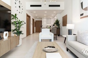 A modern living room with a sofa, a coffee table, and a TV. There is a plant and a lamp on the side. - Luxury 1BR Haven - Prime Location - Newly Built (Dubai)