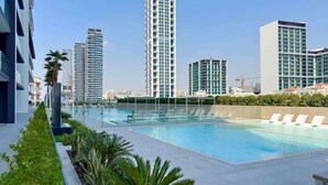 Piscina en la azotea con sillones de descanso, rodeada de edificios altos y vegetación.