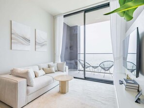 A modern living room with a sofa, a coffee table, and a balcony with chairs. - Brand New, Luxury Furnished, 1BR Apartment in JVC (Dubai)