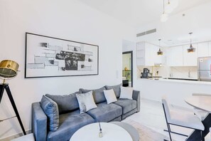 Ein modernes Wohnzimmer mit einer grauen Couch, einem runden Couchtisch und einem Essbereich mit weißen Stühlen.
