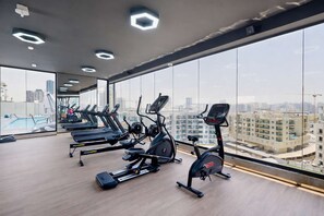 Ein Fitnessstudio mit Laufbändern, Crosstrainern und Rudergerät, große Fenster mit Blick auf die Stadt.