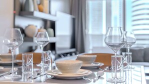 A dining table set with clear glassware and white bowls, with a modern interior and a view of the city through large windows. - Pool View, Fully Furnished, Prime Location! (Dubai)