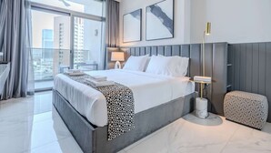 A modern hotel room with a large bed, a bedside table, a lamp, and a view of the city through the window. - Pool View, Fully Furnished, Prime Location! (Dubai)