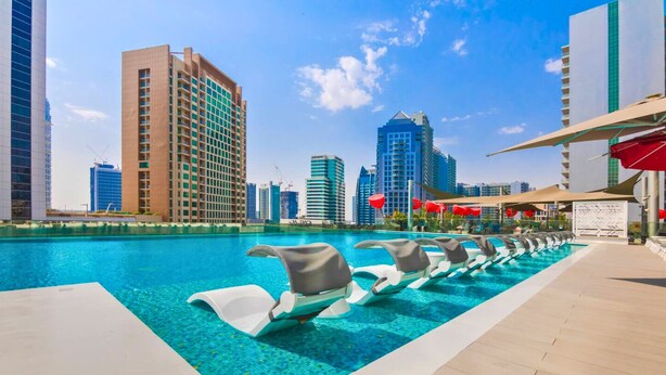 A swimming pool with lounge chairs, surrounded by high-rise buildings and a clear sky. - Pool View, Fully Furnished, Prime Location! (Dubai)