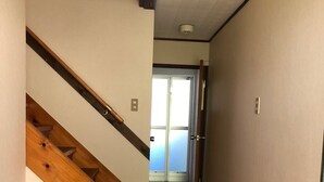 Una escalera de madera con una lámpara arriba, que conduce a un pasillo con una puerta y vista de un edificio.