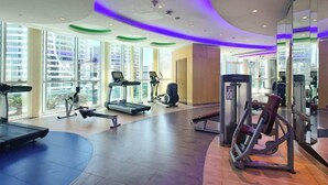 Une salle de sport moderne équipée de tapis de course, de vélos elliptiques et de matériel de musculation.