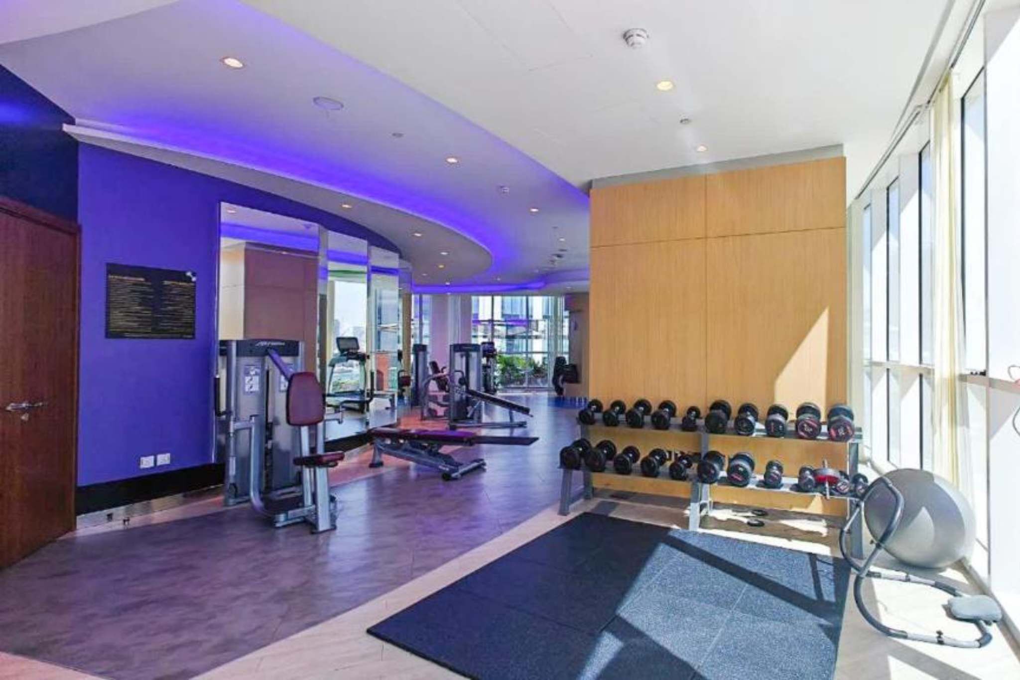 Et fitnesscenter med træningsudstyr, en væg med håndvægte og et stort vindue, der giver naturligt lys.