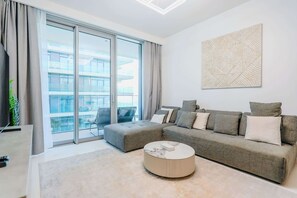 Ein modernes Wohnzimmer mit einem grauen Sofa, einem runden Couchtisch und einem großen Fenster mit Blick auf ein Gebäude.