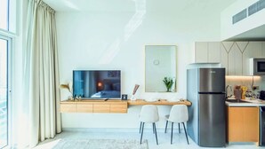 Een moderne woonkamer met een televisie, een eethoek met twee stoelen, een keuken met een koelkast en een groot raam met gordijnen.
