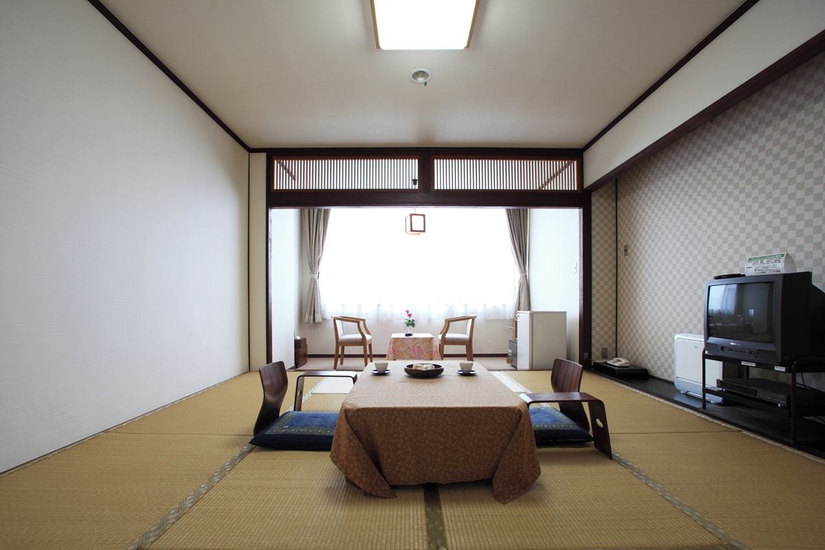A traditional Japanese room with tatami flooring, a low table with cushions, a television, and a view through a shoji screen.