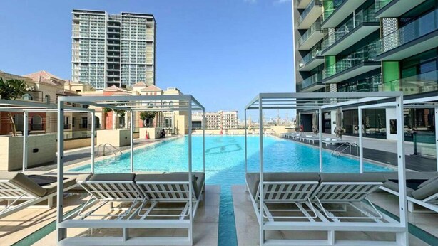 Una piscina con sillas de descanso, rodeada de edificios modernos.
