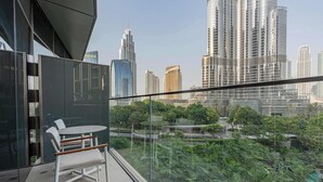 A balcony with a glass railing, a table, and chairs, overlooking a cityscape with tall buildings and greenery. - Full Burj Khalifa View, Luxury 3BR Unit, Downtown (Dubai)