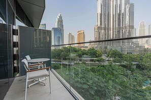 Ein Balkon mit Glasgeländer, Tisch und Stühlen mit Blick auf eine Stadtlandschaft aus hohen Gebäuden und Grünflächen.