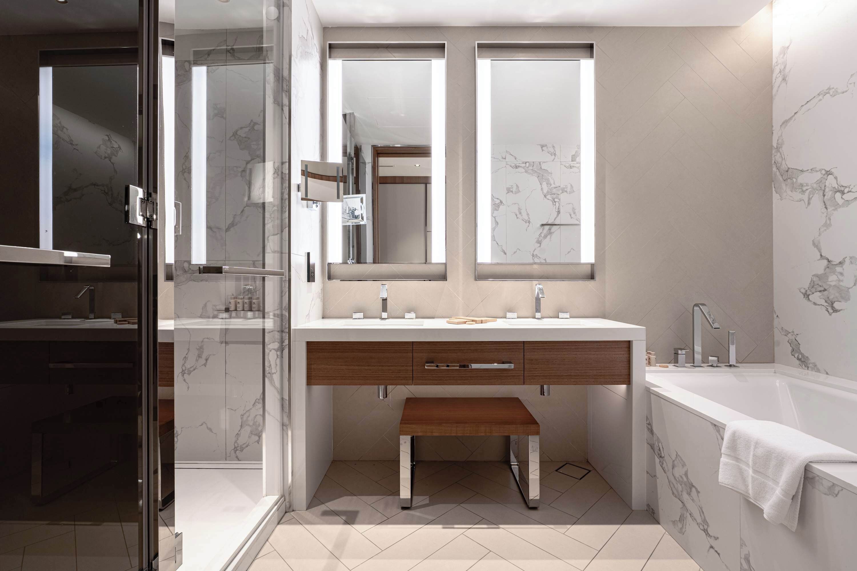 A modern bathroom with a glass shower enclosure, a vanity with a marble backsplash, and a freestanding bathtub.