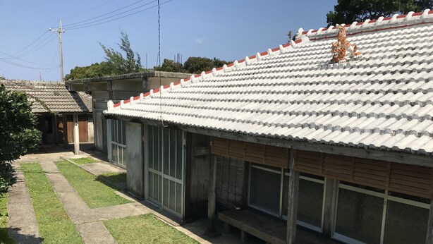 Un bâtiment doté d’un toit en tuiles, de grandes fenêtres et d’une cour dallée.