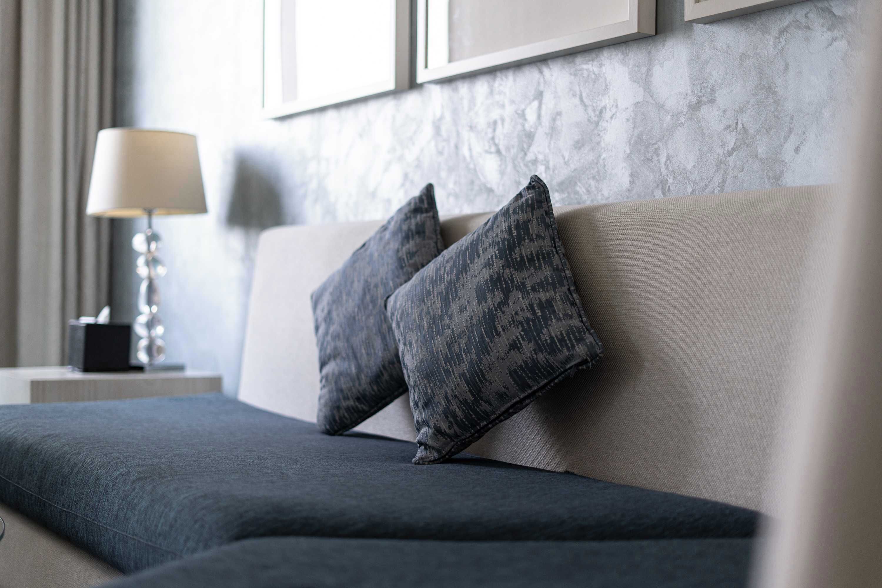 A modern hotel room with a sofa, two pillows, a lamp, and a framed picture on the wall.