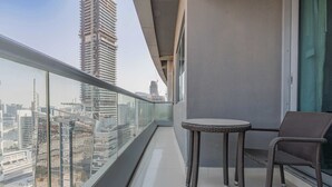 Un balcon doté d’une balustrade en verre, une table ronde et un fauteuil en osier, offrant une vue sur un paysage urbain avec de hauts immeubles.