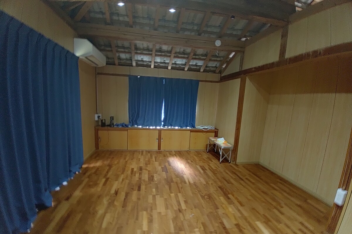 A room with wooden flooring, a blue curtain, a small table, and a cabinet.