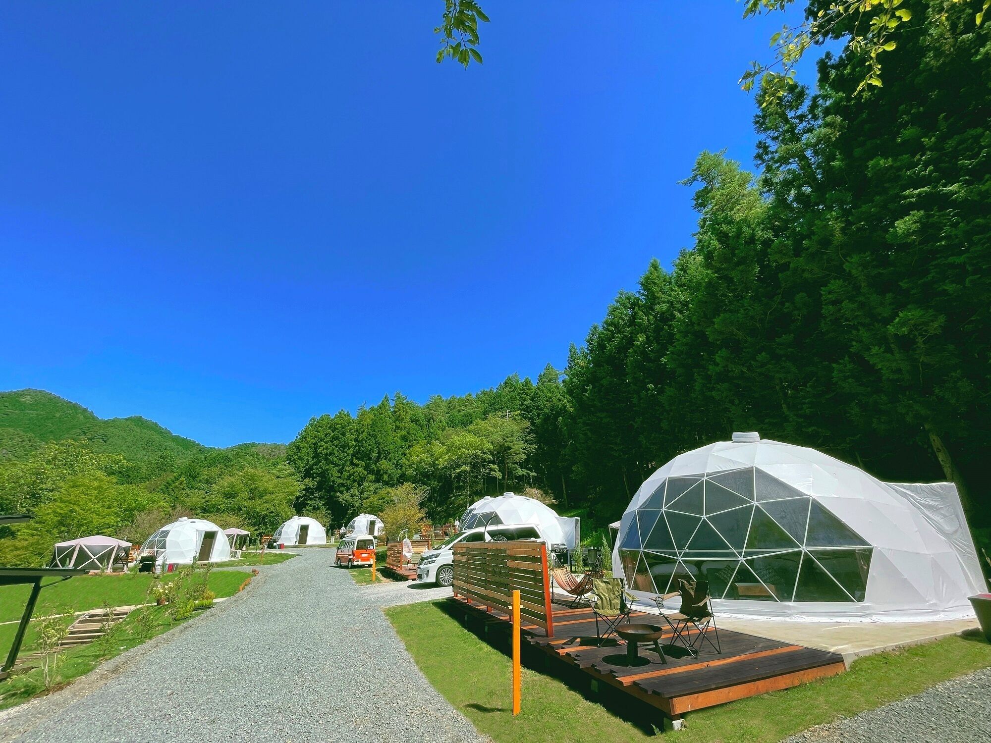 A campsite with geodesic dome tents, a gravel path, and a wooden deck with seating.