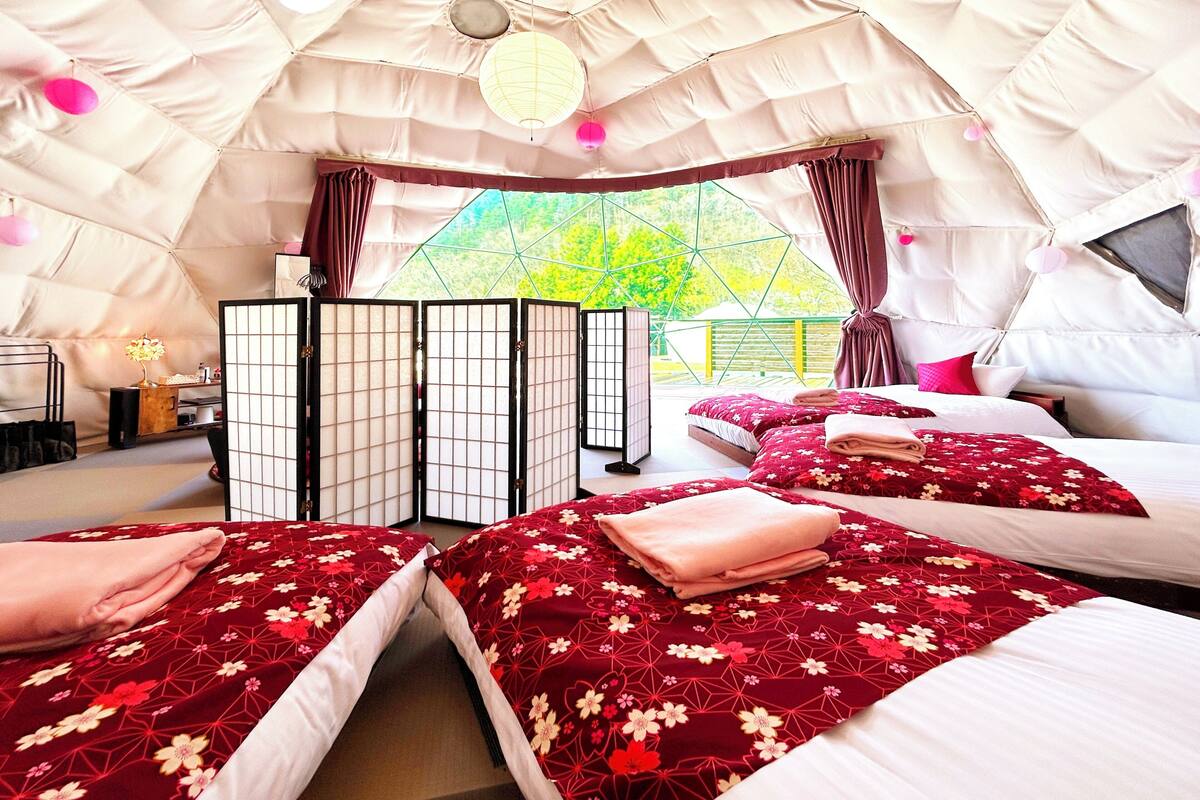 Una habitación tipo tienda de campaña acogedora y bien iluminada, con dos camas, un panel japonés tradicional y vistas a la vegetación.