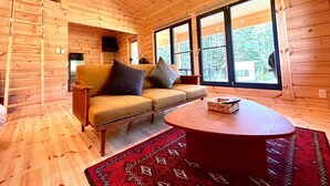 Een houten interieur met een bank, een ronde tafel en grote ramen.
