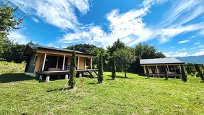 Een tweelaags gebouw met een veranda, omringd door gazon en bomen, onder een heldere lucht.