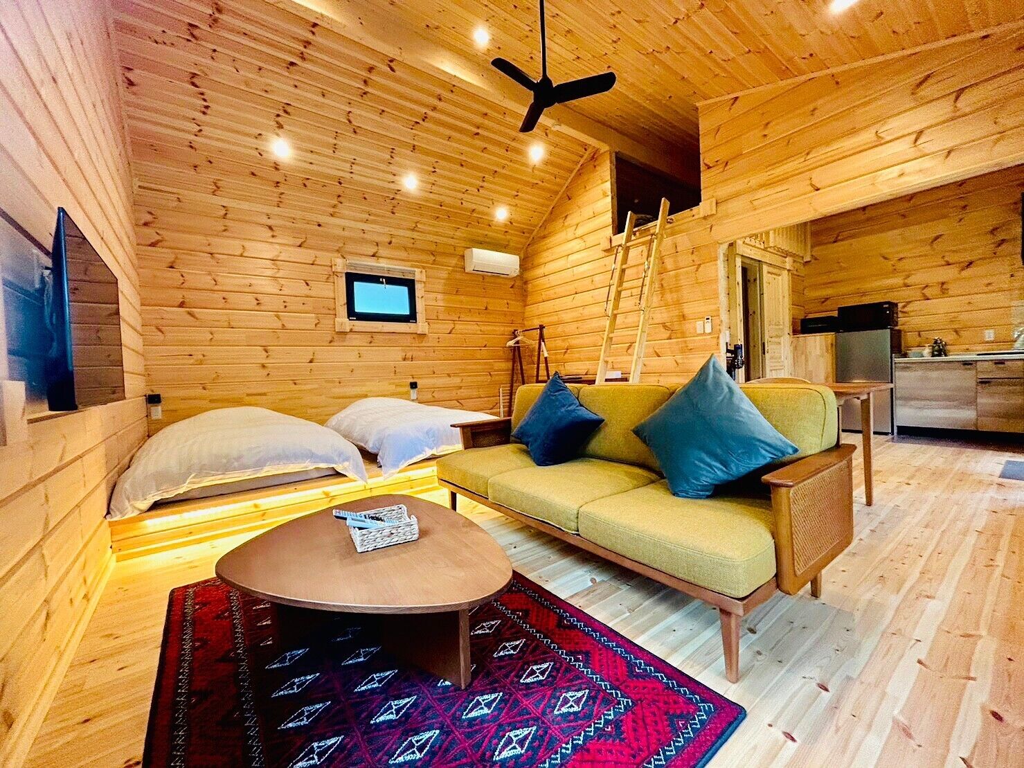 A cozy log cabin interior with a sofa, two beds, a dining area, and a kitchen.