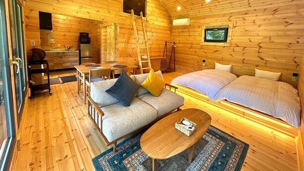 Een knus interieur van een blokhut met een bank, een bed, een eettafel en een keukenhoek.