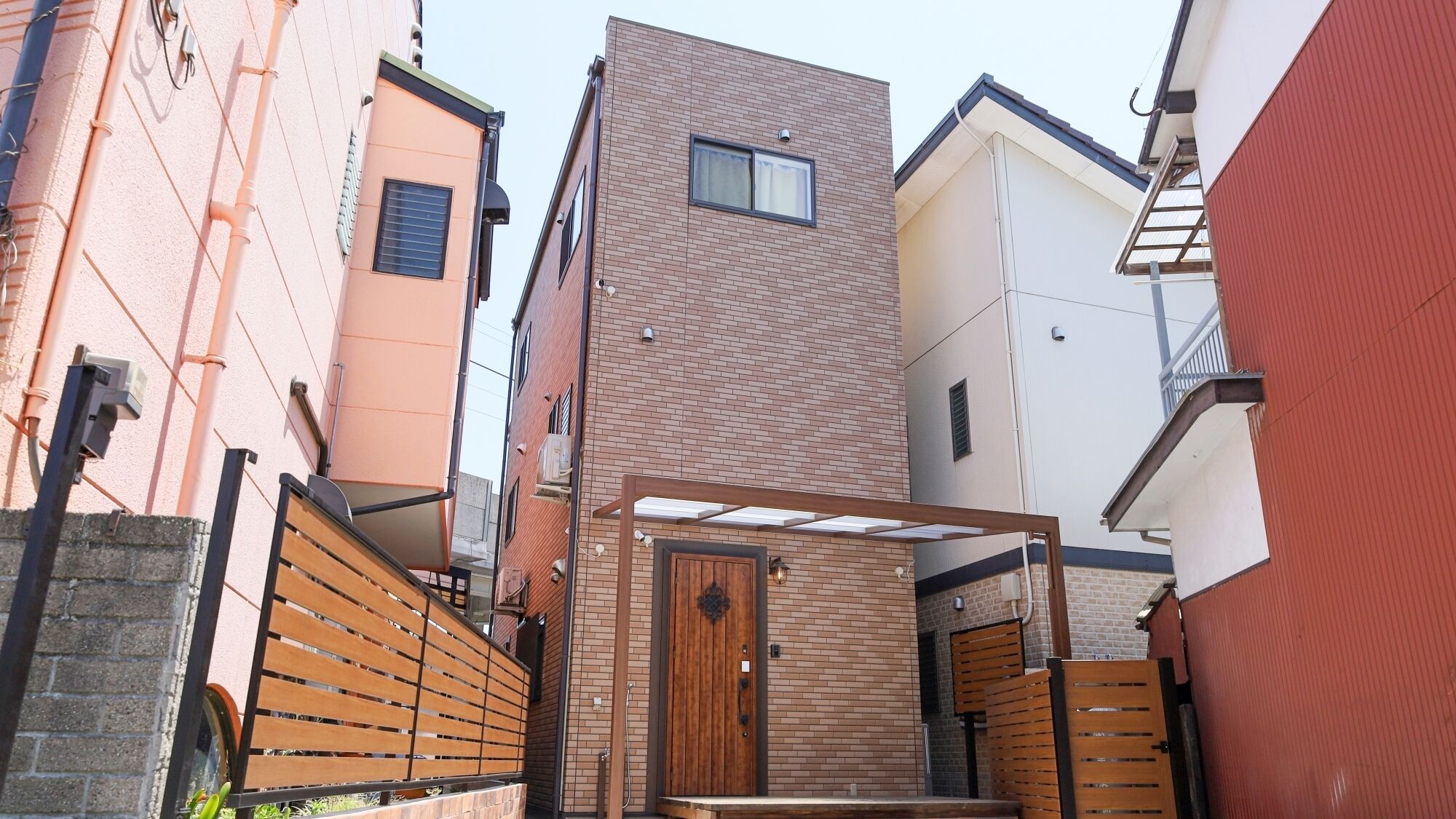 A narrow urban alleyway with a wooden gate, a small wooden door, and a brick building with a window.