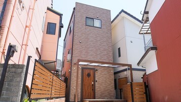 Un estrecho callejón urbano con una verja de madera, una pequeña puerta de madera y un edificio de ladrillo con un ventanal.