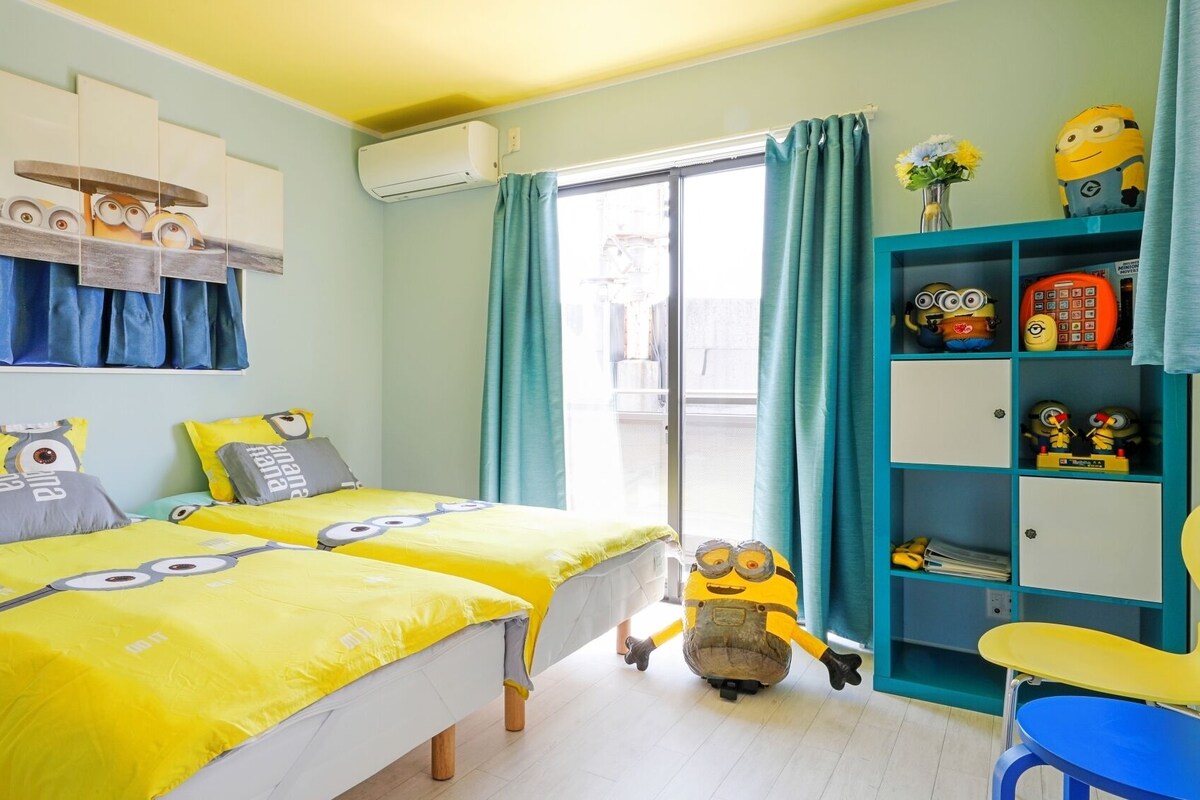 A room with two beds, a desk, a chair, and a Minion-themed decor.