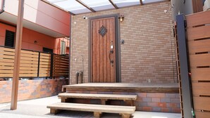 Una puerta de madera con un picaporte de metal, un muro de ladrillo y un banco de madera afuera.
