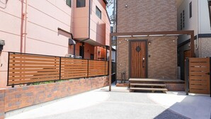 Una entrada con portón, un banco de madera, un muro de ladrillo y un edificio con puerta de madera.