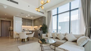A modern living room with a sofa, coffee table, and dining area. There is a large window providing natural light and a view of the city. - Luxury 2BR Getaway - Prime Location in Meydan (Dubai)