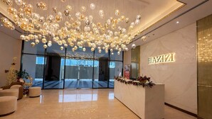 A modern hotel lobby with a marble reception desk, a large chandelier, and a glass entrance. - Luxury 2BR Getaway - Prime Location in Meydan (Dubai)