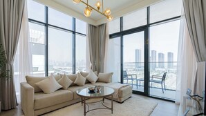 A modern living room with a beige sofa, a glass coffee table, and a large window offering a city view. - Luxury 2BR Getaway - Prime Location in Meydan (Dubai)