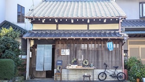 Un bâtiment japonais traditionnel, avec un toit recouvert de tuiles, une porte d’entrée en bois et un vélo garé à l’extérieur.