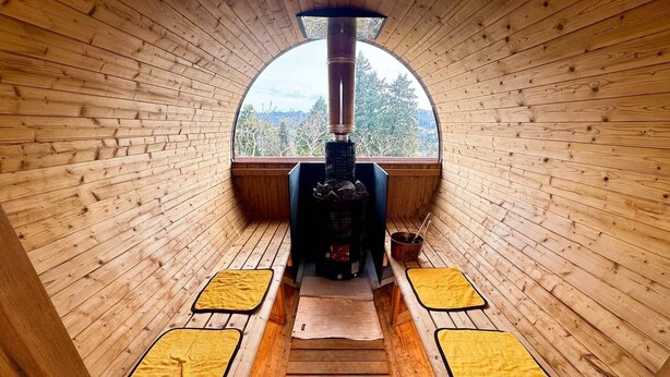 A wooden cabin interior with a central wood-burning stove, a window, and a bench. - Green Hotel Ibusuki (Misato)