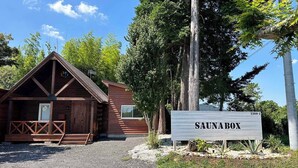A wooden cabin with a triangular roof, a wooden deck, and a sign labeled 'SAUNABOX'. - Green Hotel Ibusuki (Misato)