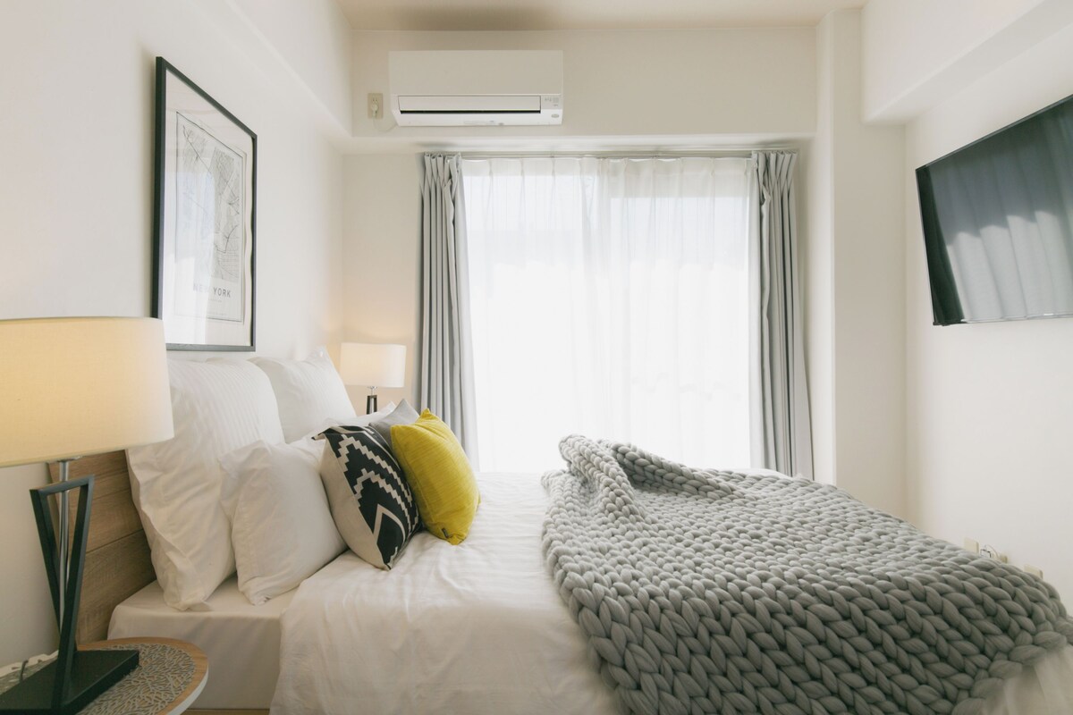 A hotel room with a bed, a bedside lamp, a framed picture on the wall, and a window with curtains.