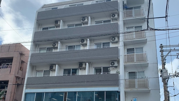 A multi-story building with balconies, air conditioning units, and a ground-level entrance. - Kin-con-kan (Naha)