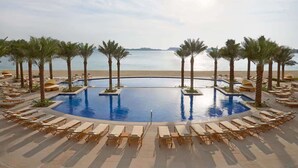 Zona de piscina amb gandules i palmeres, envoltada d'una platja i vista a l'oceà.