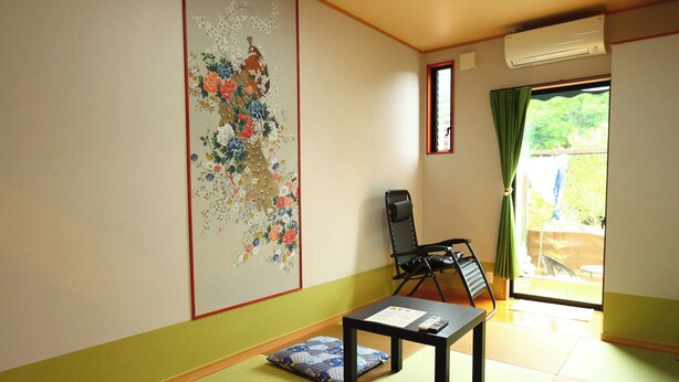 A room with tatami flooring, a black chair, a small table with a remote control, and a large floral artwork on the wall.