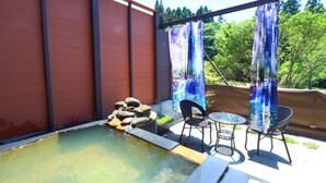 A hot tub with a waterfall feature, surrounded by rocks and a small table with chairs.